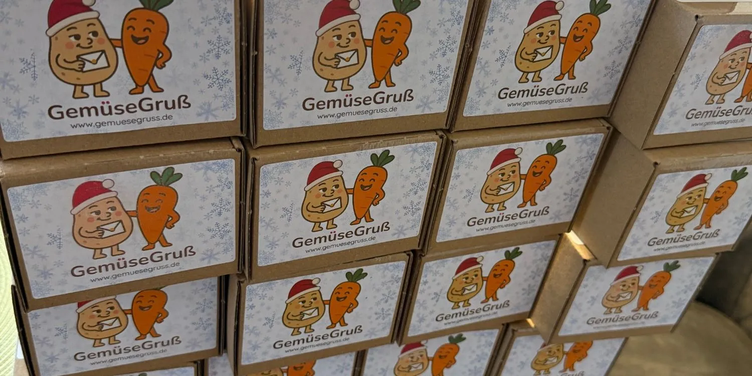 Ein Stapel versandfertiger GemüseGruß-Kartons mit Weihnachtsetikett: Kartoffel mit Weihnachtsmütze und Möhre